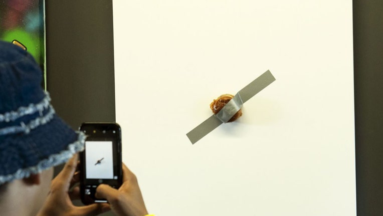 The piece, officially named “The Sandwich,” is listed at $120,003.99 and is being described as “a mixed media work of art consisting of a toasted brioche bun, two pickles, fried chicken, mayo and duct tape over a canvas.”
