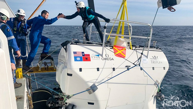 A safety swimmer (right) helps a crew member to board the submarine Limiting Factor during the Mediterranean Sea trials in January 2020 for the upcoming First Descent: Midnight Zone mission in the Indian Ocean.