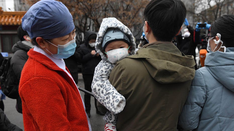 A nurse (L) looks at a 1-year-old boy as his father and mother (R) speak to the media during a ceremony marking their release after recovering from the COVID-19 coronavirus at the Youan Hospital in Beijing on Feb. 14, 2020. (Photo by GREG BAKER/AFP via Getty Images)