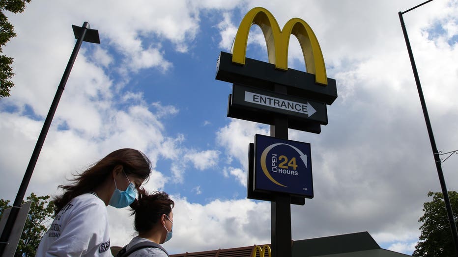Women wearing face masks walks past a McDonald's logo