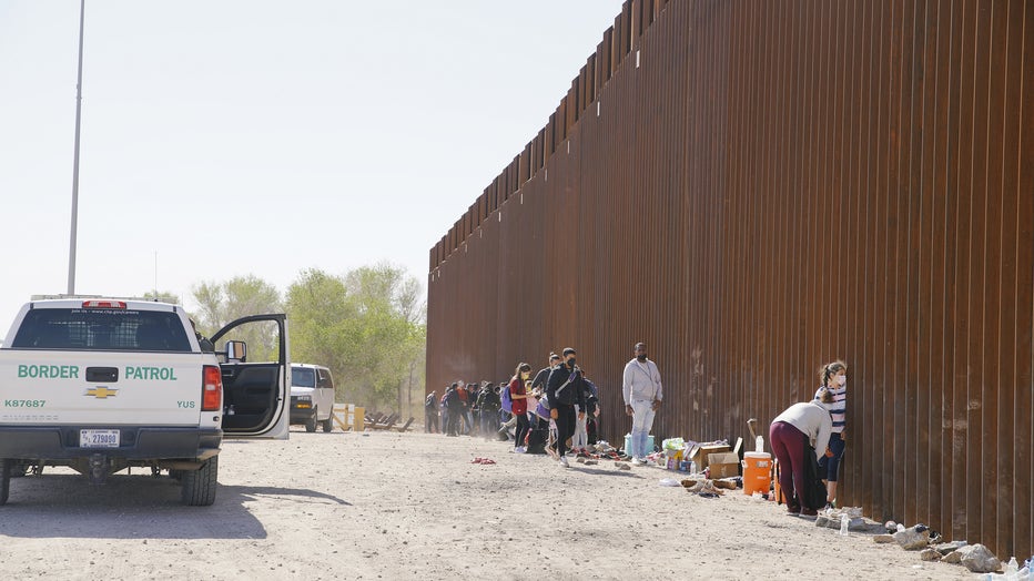 Asylum seekers from Colombia, Venezuela, and Cuba wait next to the USA border wall with Mexico, to be processed by CBP on February 21, 2022 in Yuma, Arizona, United States.