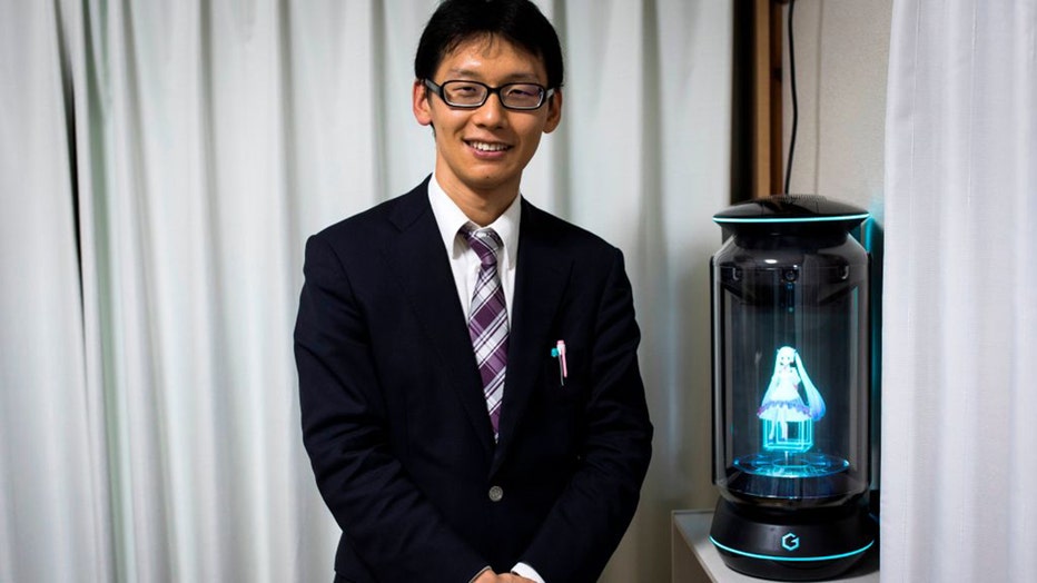 In this photograph taken on November 10, 2018 Japanese Akihiko Kondo poses next to a hologram of Japanese virtual reality singer Hatsune Miku at his apartment in Tokyo, a week after marrying her.
