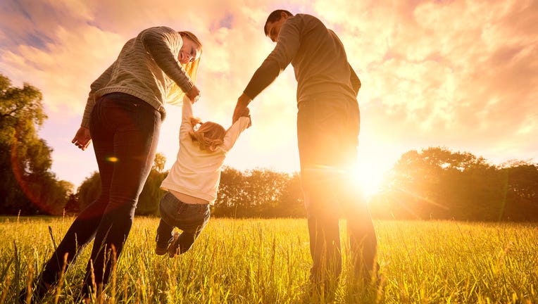 Parents hold baby's hands. Happy family in park evening