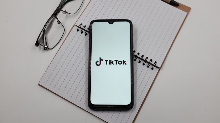 In this photo illustration a TikTok logo is displayed on a smartphone screen above a notebook next to glasses. (Photo Illustration by Nikolas Kokovlis/NurPhoto via Getty Images)
