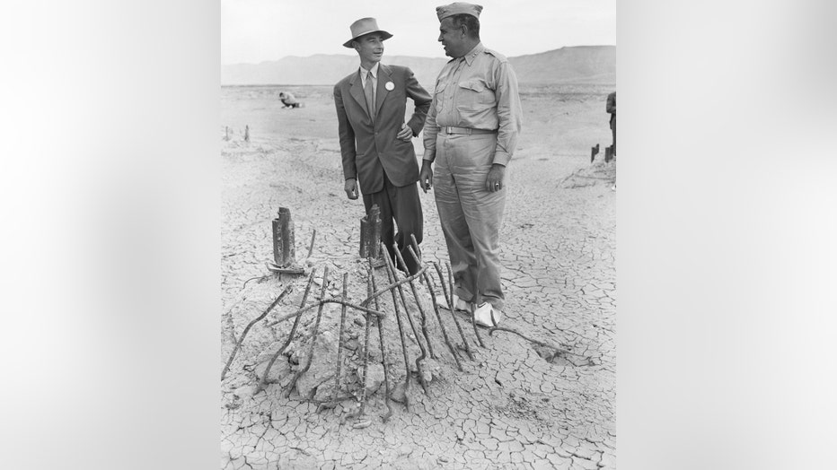 Maj. Gen. Leslie R. Groves (right), Chief of Manhattan Engineering District in which first Atomic Bomb was developed, and Dr. J. R. Oppenheimer, Director of Los Alamos Atomic Bomb Project and Physicist at California Technological Institute, view the base of the steel tower on which first atomic bomb hung when tested near Alamogordo in July. The intense heat of the bomb melted the tower, and seared the surrounding sands into Jade green Glasslike cinders. (Getty)
