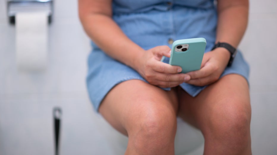 A woman holds her smartphone in her hands on the toilet. (Photo by Robert Michael/picture alliance via Getty Images)