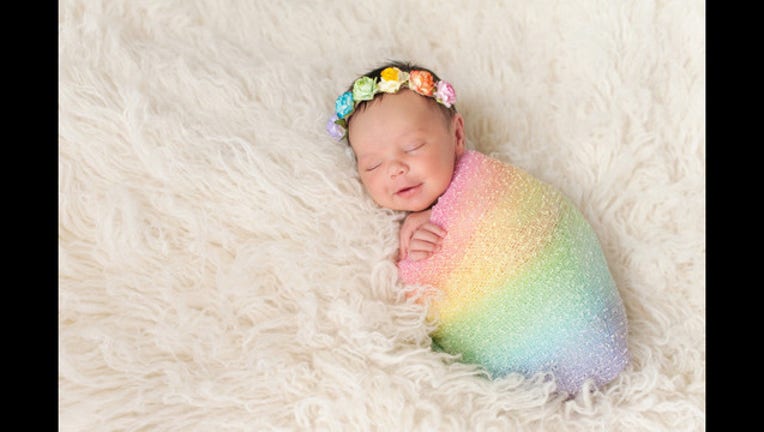 915460b7-Smiling Newborn Baby Girl Wearing a Rainbow Colored Swaddle_1457797752996-404959