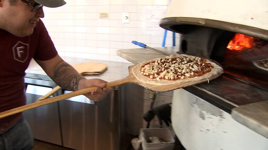 Photo: Employee placing pizza in wood-fired stove