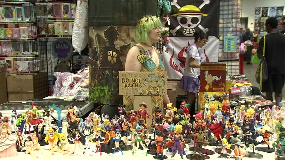A woman standing with a table of figurines at Tampa MetroCon 2022. 