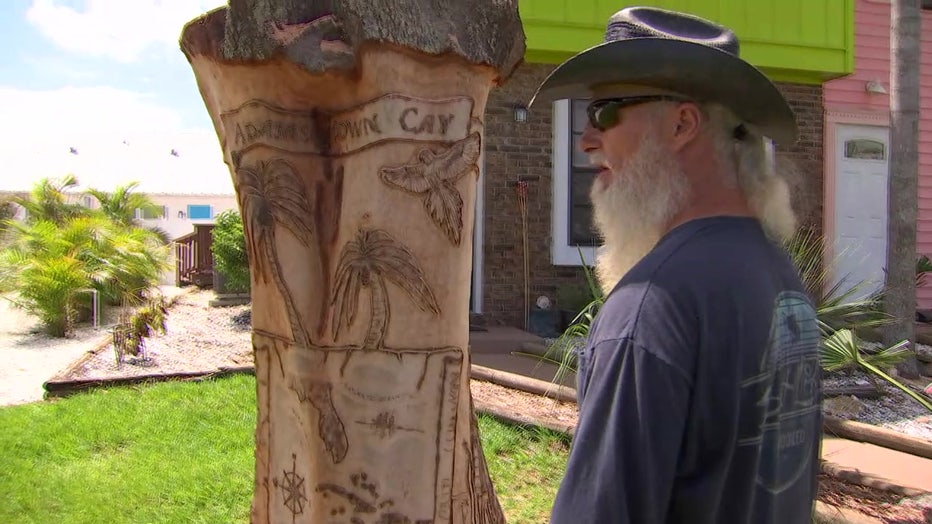 Pastor Ray Gibbons next to tree with art he carved. 