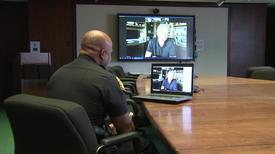 Officer Bradley Hill at conference table and Gary Sinise on video call. 
