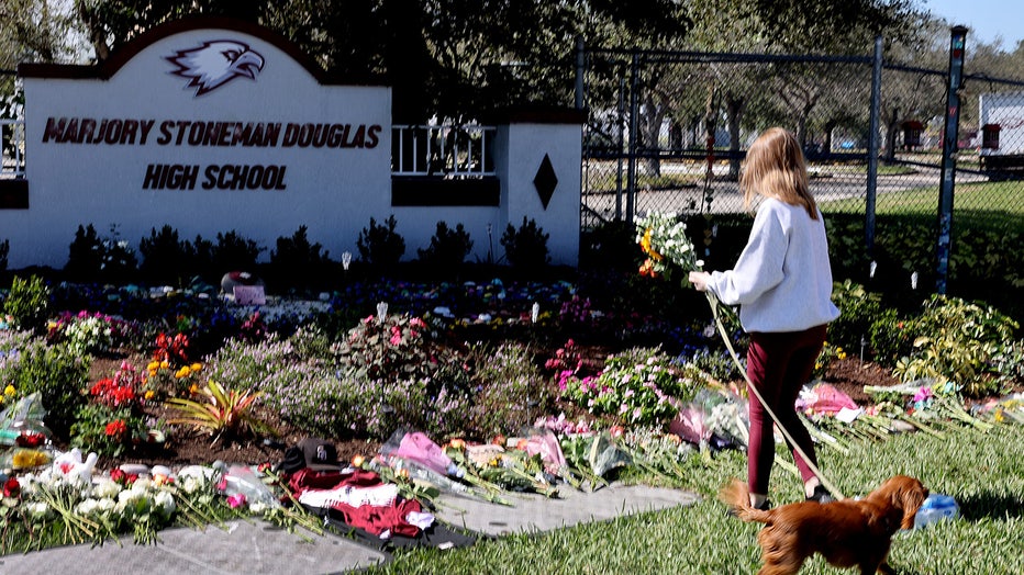 Photo: Photo: Emma Cabak places flowers on a memorial in front of Marjory Stoneman Douglas High School to honor those killed during a mass shooting on February 14, 2022 in Parkland, Florida.