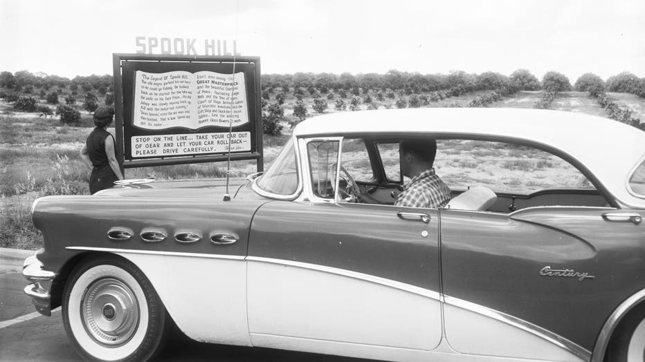 A couple reads a sign displaying the legend of Spook Hill - Lake Wales, Florida in 1956. Courtesy of the Florida Memory Project.