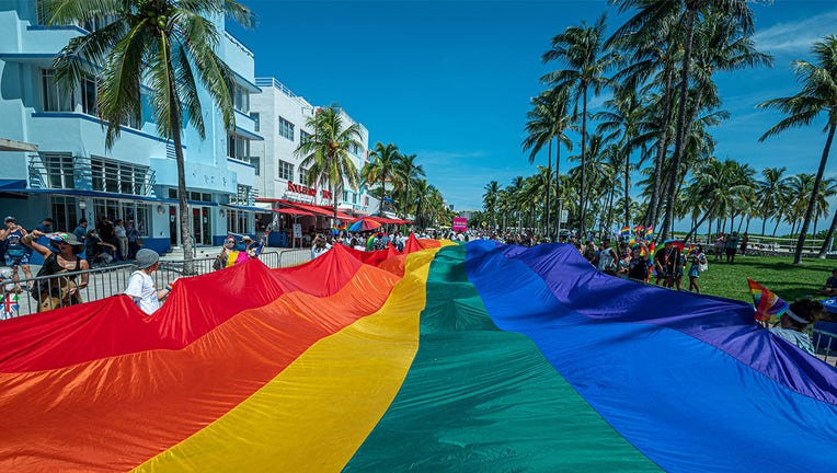 A huge multi-colored flag flies over Ocean Drive as people participate in the Pride Parade, during the Miami Beach Pride Festival, in Lummus Park, South Beach, Florida on September 19, 2021.