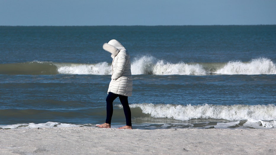 A woman in a parka walks along the sand in St. Pete Beach.
