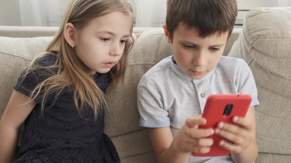 Two children look at a cell phone. 