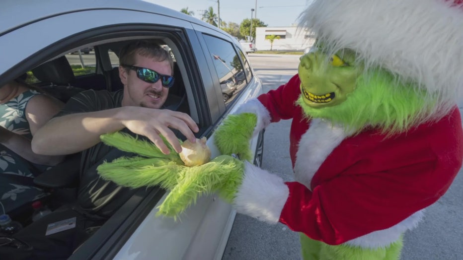 In this photo provided by the Florida Keys News Bureau, a Maryland motorist, left, accepts an onion instead of a traffic citation from Monroe County Sheriff's Office Colonel Lou Caputo, right, costumed as the Grinch, Tuesday, Dec. 13, 2022, in Marathon, Fla. For drivers slightly speeding through a school zone on the Florida Keys Overseas Highway Tuesday, Caputo offered them the choice between an onion or a traffic citation. It's a holiday tradition in the Keys that Caputo began 20 years ago to educate drivers that Keys schools remain in session through Dec. 16. 