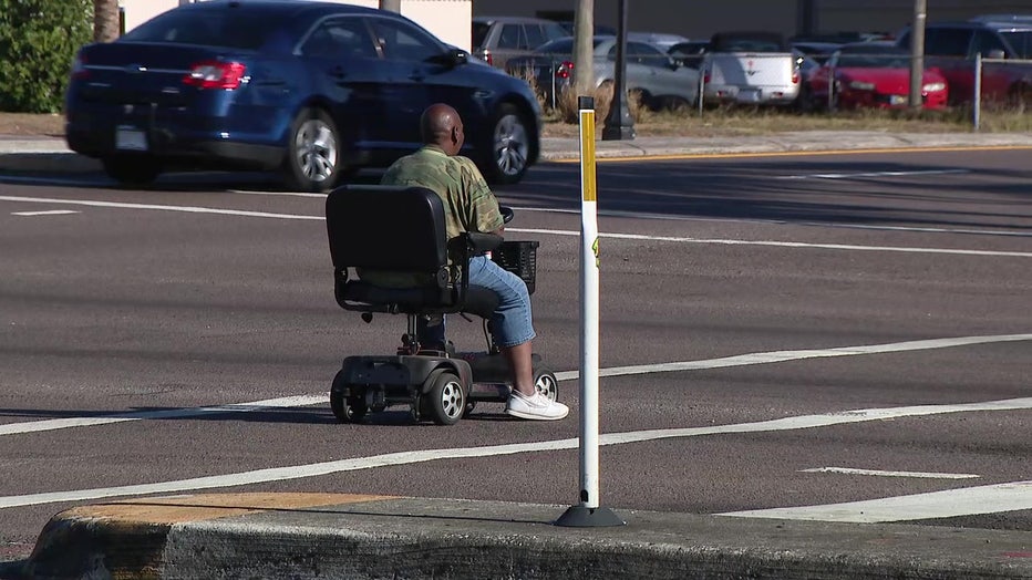 A man crosses a Polk County street on a motorized scooter.