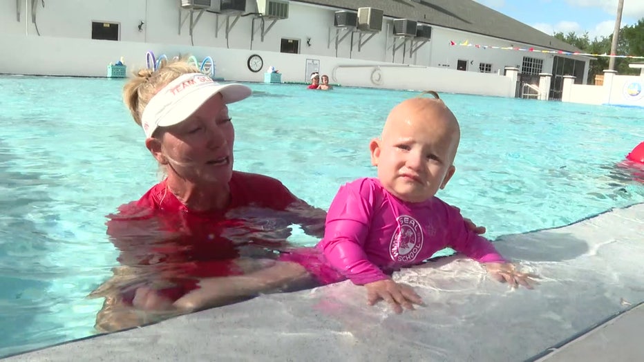 An instructor helps a baby gets out of the pool. 