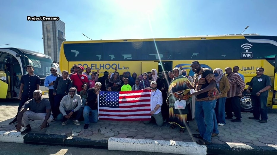 Americans pose with American flag outside of bus after being rescued by Project Dynamo. 