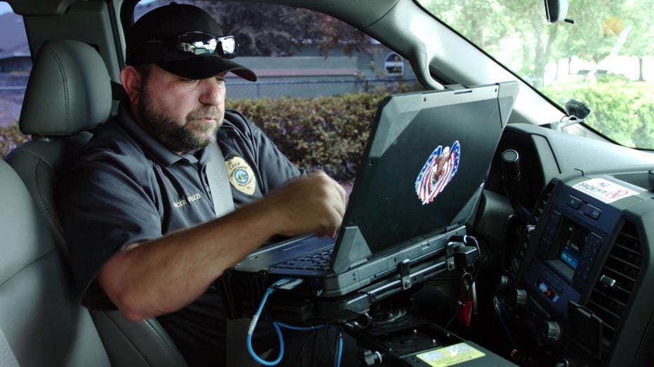 A Pasco County code compliance officer in a vehicle using a computer .