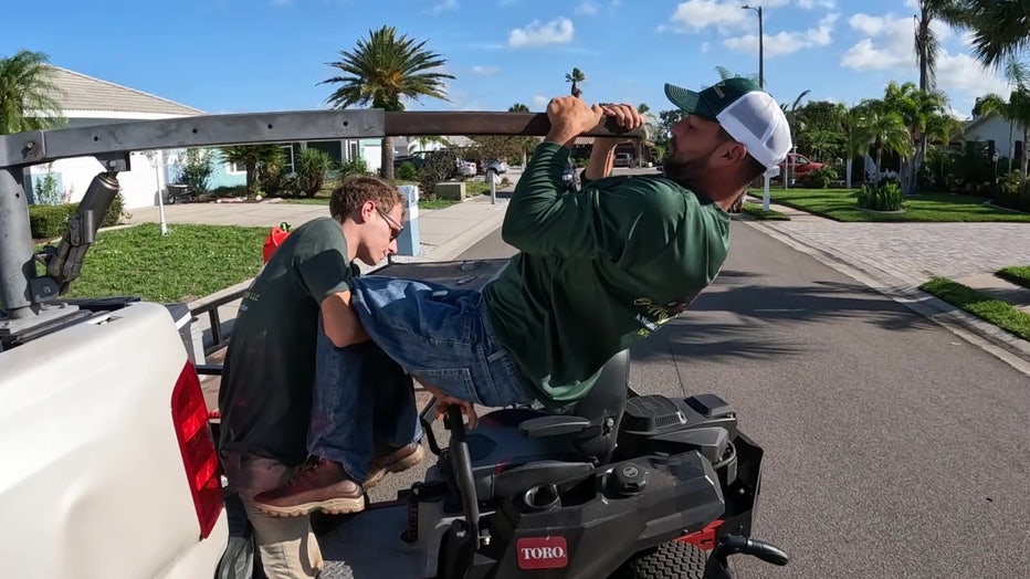 Jared Ramella's nephew helps him get onto the lawn mower. 