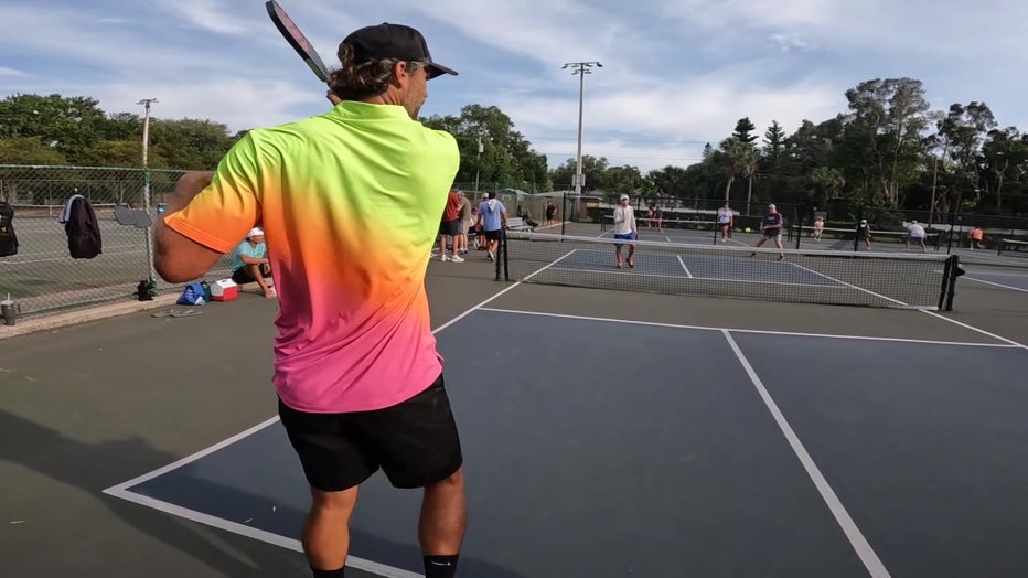 Pickleball players play on outdoor court.