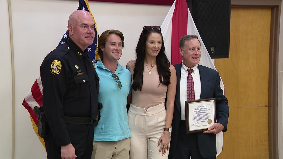 Charles McKeon and the woman he saved pose for photo with the award and law enforcement.