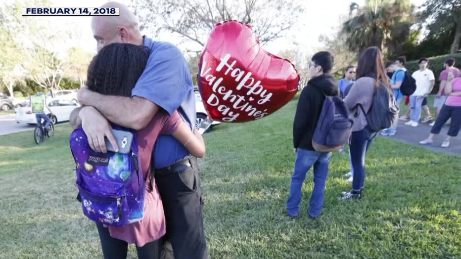 A student holds a Valentine's Day balloon while hugging a parent after a school shooting. 