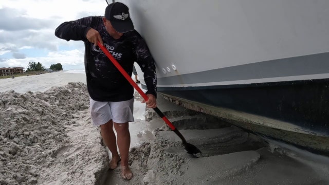 Man works to move derelict boat that washed ashore in Treasure Island after severe storms