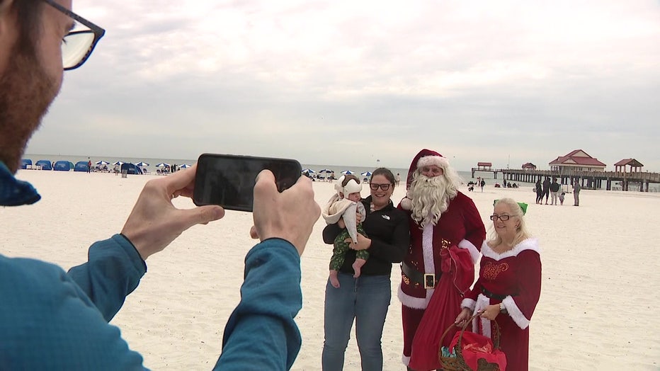 Gary and Jennifer Seguin are taking pictures with people on the beach in Clearwater dressed as Santa and Mrs. Claus.