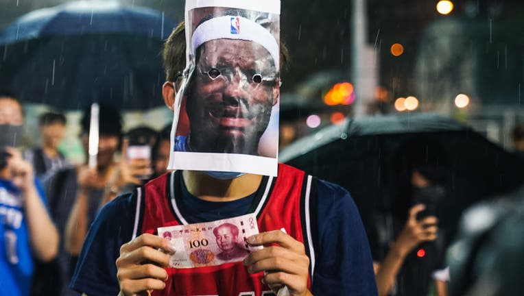 HONG KONG, CHINA: A basketball fan wearing Miami Heat jersey with a Lebron James mask on licking a 100 Chinese yuan bill on October 15, 2019 in Southorn Playground, Wan Chai, Hong Kong, China. Anti-government demonstrations in Hong Kong stretched into its fifth month after the Chinese territory's government invoked emergency powers earlier this month to introduce an anti-mask law. Protesters continue to call for Hong Kong's Chief Executive Carrie Lam to meet their remaining demands since the controversial extradition bill was withdrawn, which includes an independent inquiry into police brutality, the retraction of the word 