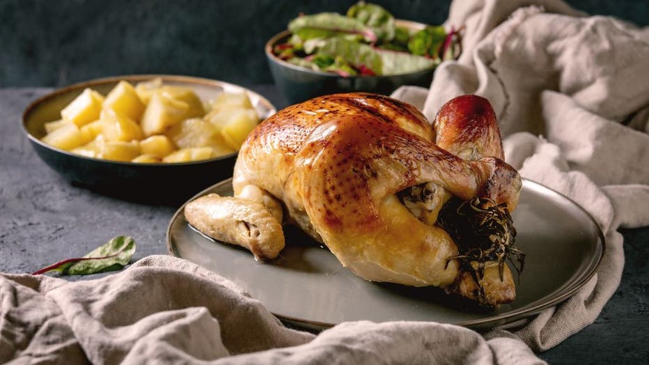 Whole baked chicken poultry on ceramic plate served with potatoes and young beetroot salad leaves over black concrete background with linen cloth. Dinner menu