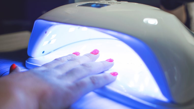 Female Hand with red nails in the lamp for manicure. Nail Lamp Dryer for Gel Nail Polish Curing Manicure Pedicure.