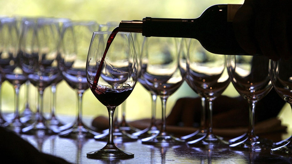 Bottle of red wine is poured into wine glasses.