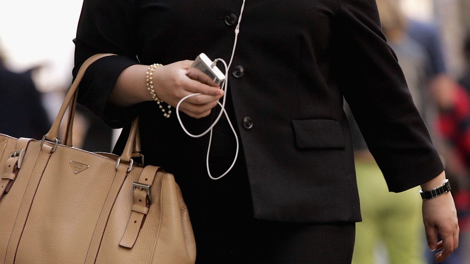 Woman walks down street holding purse and iPod.