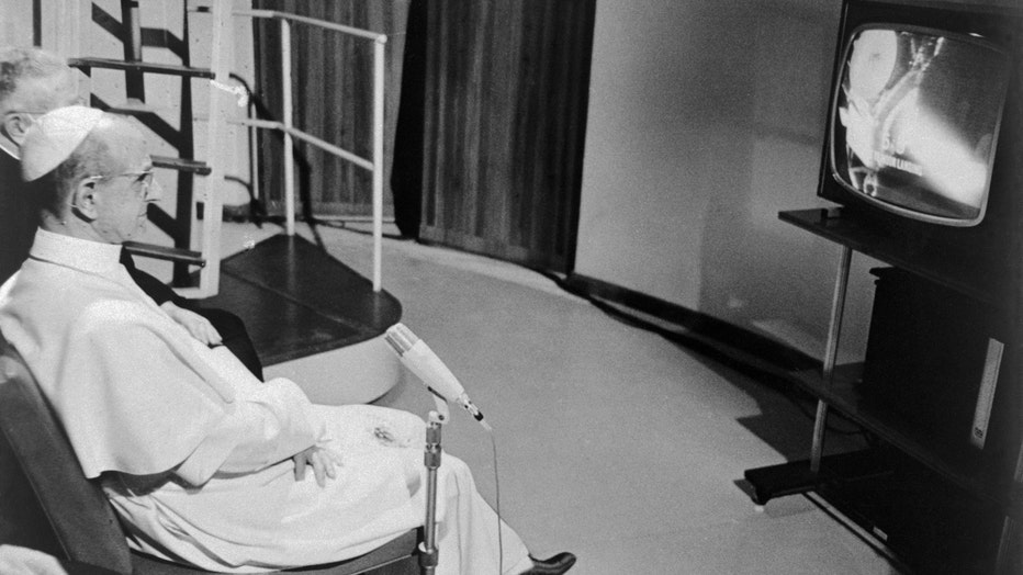 Pope Paul VI sits before a television set in his summer villa and watches the astronauts Neil Armstrong and Buzz Aldrin land on the moon.