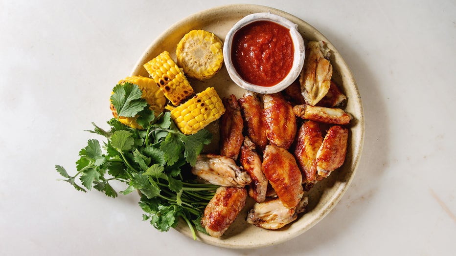 A file image shows chicken wings served on a plate with red sauce, grilled sweet corn and parsley. (Photo by: Natasha Breen/REDA&CO/Universal Images Group via Getty Images)