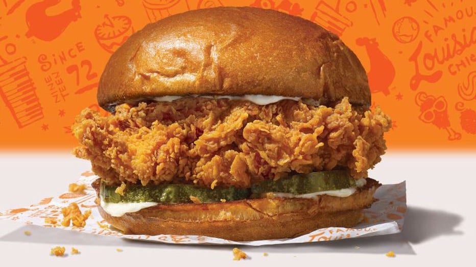 Popeyes' new chicken sandwich is shown in a promotional photo, featuring a buttermilk-battered and hand-breaded chicken filet on a toasted brioche bun, topped with pickles and either mayo or spicy Cajun spread. (Photo credit: Popeyes)
