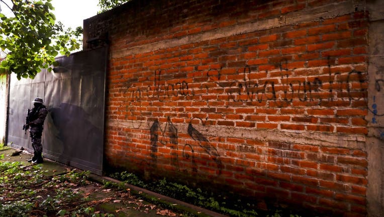 A police guard stands next to a graffiti wall with the name of a gang as part of a routine patrol in Lourdes, La Libertad, El Salvador.