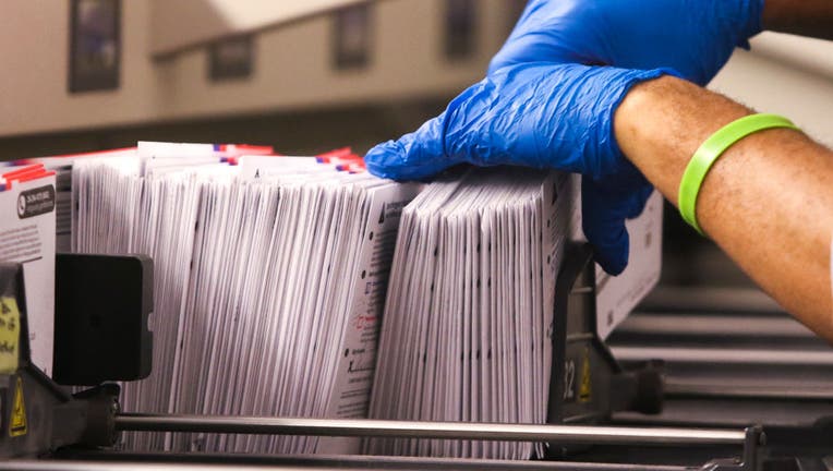 An election worker handles vote-by-mail ballots coming out of a sorting machine for the presidential primary at King County Elections in Renton, Washington on March 10, 2020.