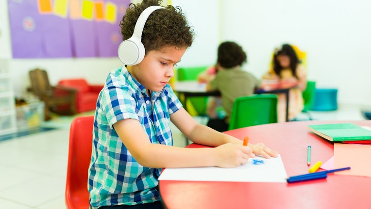 Autistic preschooler with headphones coloring alone in class