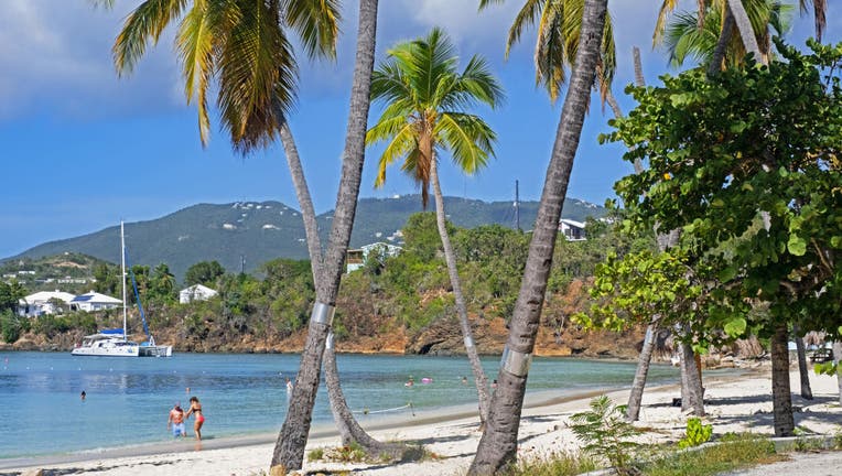 Tourists on white sandy beach with palm trees along Druif Bay at Water Island