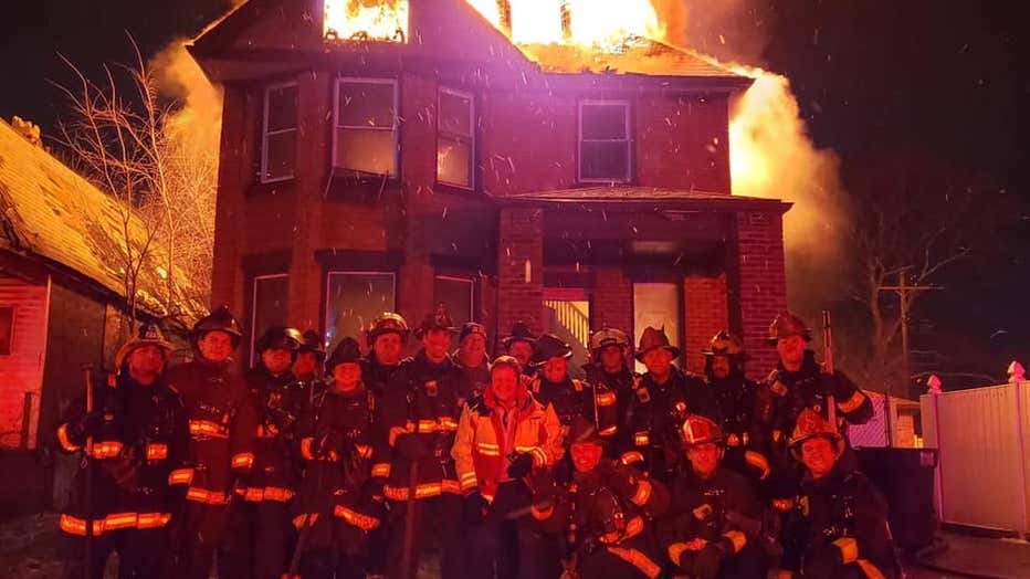 A photo of a group of firefighters in front of a raging house fire