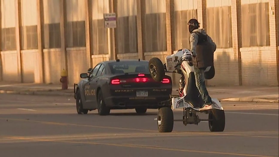 An ATV pops a wheelie behind a Detroit police squad car