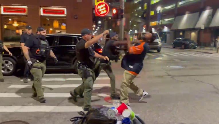 The man who was punched doesn't appear to react when officers try to lift him up. He eventually wakes up and begins shaking his hand at the police. Pedestrians then help him up as officers leave the scene.