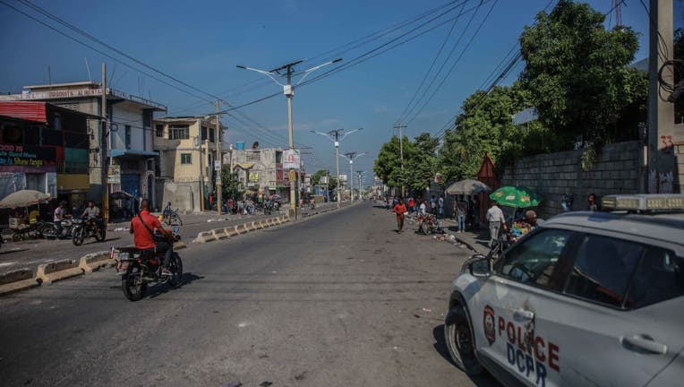 People ride a motorcycle past a police car following a call for a general strike launched by several professional associations and companies to denounce insecurity in Port-au-Prince on Oct. 18, 2021. (Photo by RICHARD PIERRIN/AFP via Getty Images)