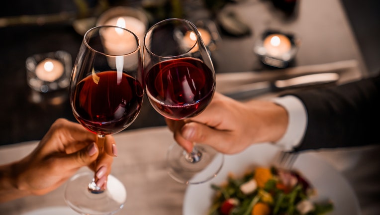 Close up of young couple toasting with glasses of red wine at restaurant