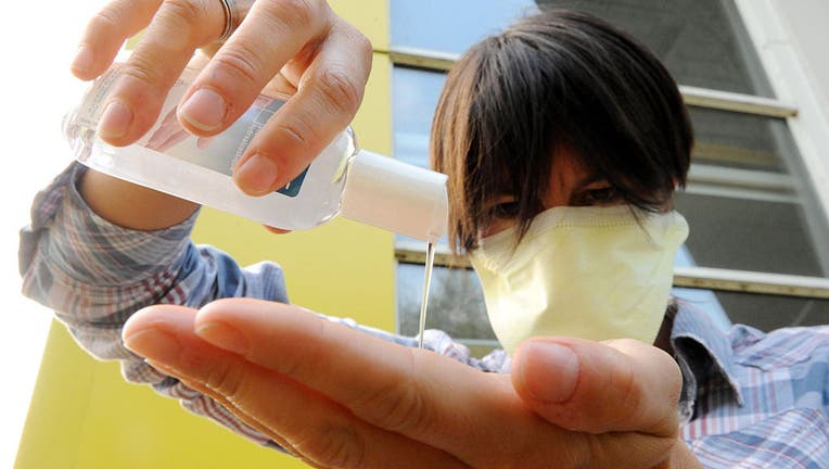 FILE - A woman wearing a surgical mask uses hand sanitizer. 