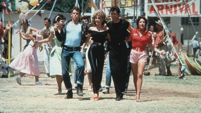 Jeff Conaway, Olivia Newton-John, John Travolta and Stockard Channing walk arm in arm at a carnival in a still from the film, 'Grease.'